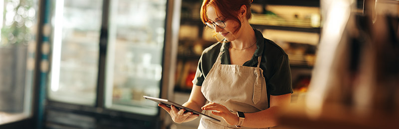 Female entrepreneur standing with an tablet computer tracking orders for her subscription box business.